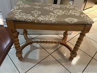 Front view of rectangular wooden bench with patterned beige upholstery and turned legs.