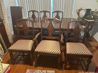 Set of six wooden chairs arranged with one armchair and five side chairs showing the detailed carved backs and upholstered patterned seats.