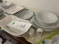 Photo showing multiple white ceramic dishes including serving bowls, casseroles, a large decorative tray, a small rectangular tray, and salt and pepper shakers arranged on a surface.