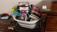 Lot items including Kirkland disposable underwear, Poise Ultra Thin Pads, and Depends disposable underwear in and around a plastic laundry basket (not included). Some packages appear open.