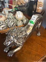 Composite lion figurine shown in side profile on wooden surface with decorative balls in background.