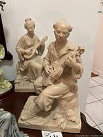 Overall view of the two figurines showing the male figurine sitting in front and the female figurine behind playing instruments on a dark wooden surface.