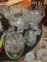 View of assorted glass and crystal vases, bowls, trays, candle holders arranged on a black table.
