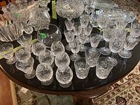 Wide view of over 25 assorted crystal and glass stemware pieces and one glass bowl arranged on a wooden table.