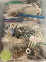 Overhead view of an assortment of jewellery making beads, clasps, and small supplies packed mostly in plastic bags and containers.