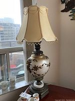 Full lamp with shade on table near window, showing overall style and height.