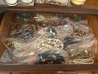 Drawer containing multiple plastic bags with various costume jewellery necklaces including imitation pearls, turquoise-colored stones, and chain styles.
