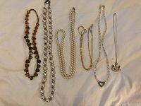 Six costume jewelry necklaces laid out flat on white background. Includes bead necklaces and chain necklaces with pendants.