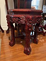 Side view of the plant stand showing detailed floral and leaf carvings on the wooden legs and apron, polished reddish wood finish.