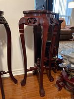 Full view of the wooden plant stand showing four cabriole legs with claw feet, carved apron details, and the square top.