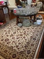 Full view of the rectangular area rug with furniture and dishes on top, showing the floral and ornate border design.