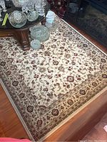 Full view of the folded rug showcasing its intricate floral and vine pattern on a light cream background with a decorative border.