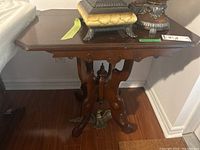 Wood table showing the front and side view of the carved pedestal base, detailing the brass eagle embellishment and the cracked tabletop.