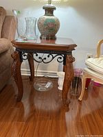 Wooden side table with lamp and glassware on top, showing full front view and carved legs under.