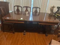 Full view of wood dining table with extension leaves closed, showing matching chairs and surrounding furniture.