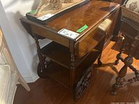 Side view of wood veneer tea cart showing drop-leaf extension and wheels.