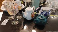 Full view of the set showing two teapots, a pitcher, and three decorative wine glasses on a reflective surface.