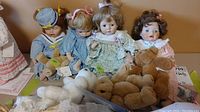 Four Ashton Drake porcelain dolls sitting in a row, each holding or accompanied by a teddy bear plush.
