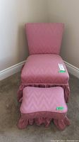 Full view of vintage pink upholstered chair with matching ottoman, showcasing gathered skirt detail and upholstery pattern.