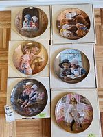 Six collector plates in original boxes arranged on a wooden floor showing the Scenes on each plate clearly