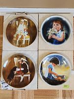 Four collector plates displayed with original boxes featuring images of children and pets in painted scenes.