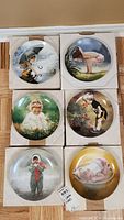 Six collector plates arranged in original box holders on wood floor, showing each unique child scene on plate front.