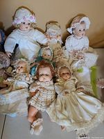 Group of nine dolls including 6 porcelain and 3 plastic dolls of varying sizes laid out together showing size and clothing variety.