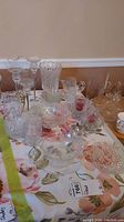 Overview of the glassware collection on a floral tablecloth, showing pitcher, candle holders, bowls, and swan dishes