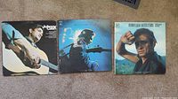 Three Johnny Cash vinyl record albums laid out on floor showing front covers with Johnny Cash playing guitar and in the outdoors.