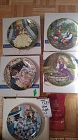 Five Kaiser collector plates displayed on the floor with boxes, showing varied fairy tale scenes with gold rims.