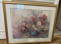 Framed floral print showing vintage bouquet with various flowers in blue vase, matted and behind glass in gold-tone frame.