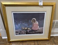 Framed limited edition print showing a young girl sitting on rocks near water with ducks