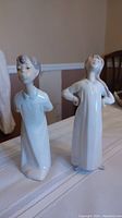 Photo of two white porcelain figurines side by side on a table, showing full height and details