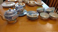 Wide view of the entire tea set on a wooden table showing teapot, sugar bowl, plates, saucers, and tea cups with hand-painted floral designs.