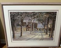 Framed winter scene art print showing a large house in snow at night with trees and lampposts.