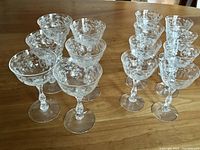 Set of all 16 Fostoria etched cocktail glasses arranged on wooden table, showing two sizes.