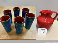 Six tall blue ceramic cups with brown interiors grouped together with a measuring tape nearby, measuring about 6 inches tall.