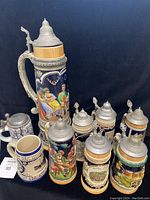 Photo showing full set of nine beer steins arranged by size, visual detail on lids and colorful ceramic work visible