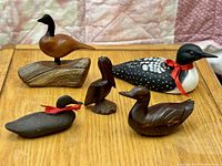 View showing all five bird sculptures arranged on a wooden surface, including the identical red ribbons on the loon and smaller duck, and various wood tones and sizes.