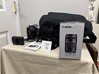 General overview of camera gear on table including camera bag, charger, manual, battery grip box, and lenses.