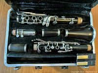 Clarinet disassembled into main parts (upper joint, lower joint, barrel, bell, mouthpiece) laid in velvet lined compartment along with two plastic reed cases containing reeds.