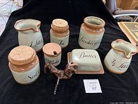 Photo showing ceramic containers for milk (1 and 3/4 liter), tea, coffee, salt, a butter dish and a corkscrew on a black background.