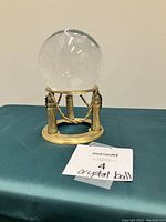 Crystal ball resting on its brass-colored decorative stand on a dark teal surface.