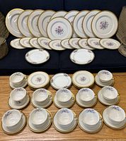 Full display of all dishes including plates, cups, and saucers arranged on a couch and floor.