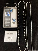 Photo showing two metallic beaded necklaces, a silver cuff bracelet and a boxed pair of blue splatter design earrings from DeCordova museum.