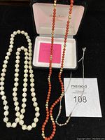 All three necklaces displayed on black background; white iridescent beads on left, coral and gold-tone beads center, silver chain with beads on right