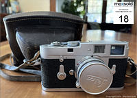 Front view of Leica M2 camera with leather case behind