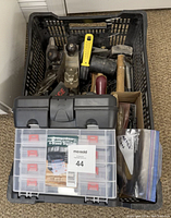 Black plastic crate filled with miscellaneous hand tools including hammers and planes with a black and translucent Wood River 4-drawer organizer on top