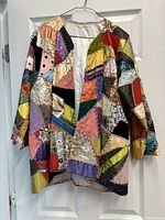 Front view of the brightly colored patchwork jacket hanging on a hanger, showing irregular embroidered fabric patches in many colors