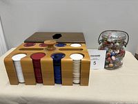 Poker chip holder with stacks of red, white, blue chips next to vintage glass jar filled with marbles.